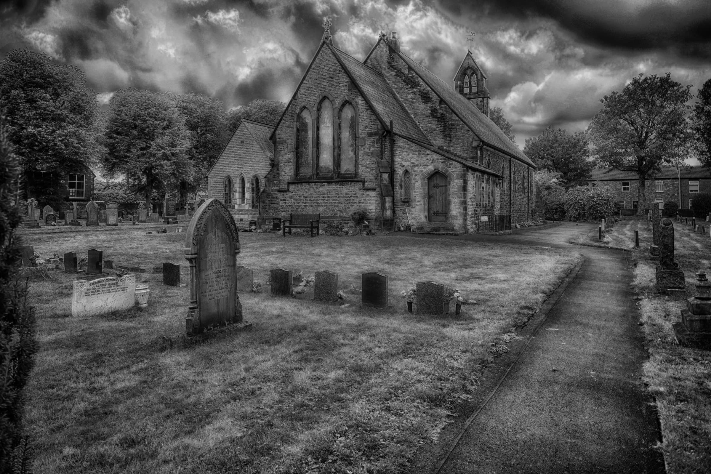 Black-and-white architectural photograph of a church in Lowton beneath dramatic clouds
